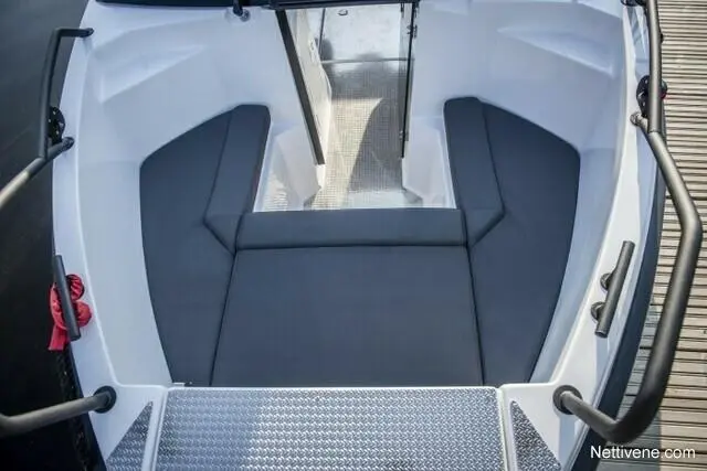 Interior of a boat showing grey cushioned seating and a metal door, with a textured step leading outside.